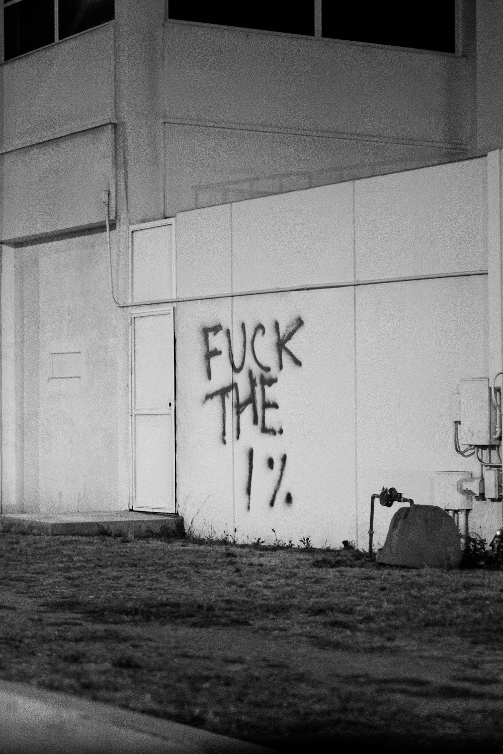 grayscale photo of man in black jacket and pants standing beside wall with graffiti