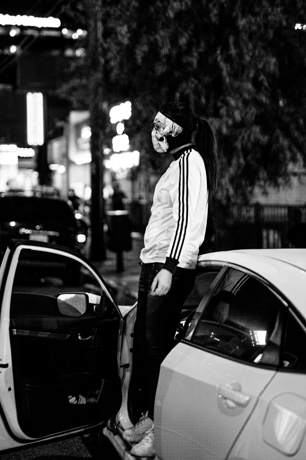 man in hoodie standing beside car in grayscale photography