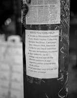 A black and white poster is taped to a pole, containing text about ways to help social justice causes. The poster mentions donating to various funds, signing petitions, getting educated on issues, and using personal privilege to speak up.