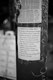 A black and white poster is taped to a pole, containing text about ways to help social justice causes. The poster mentions donating to various funds, signing petitions, getting educated on issues, and using personal privilege to speak up.