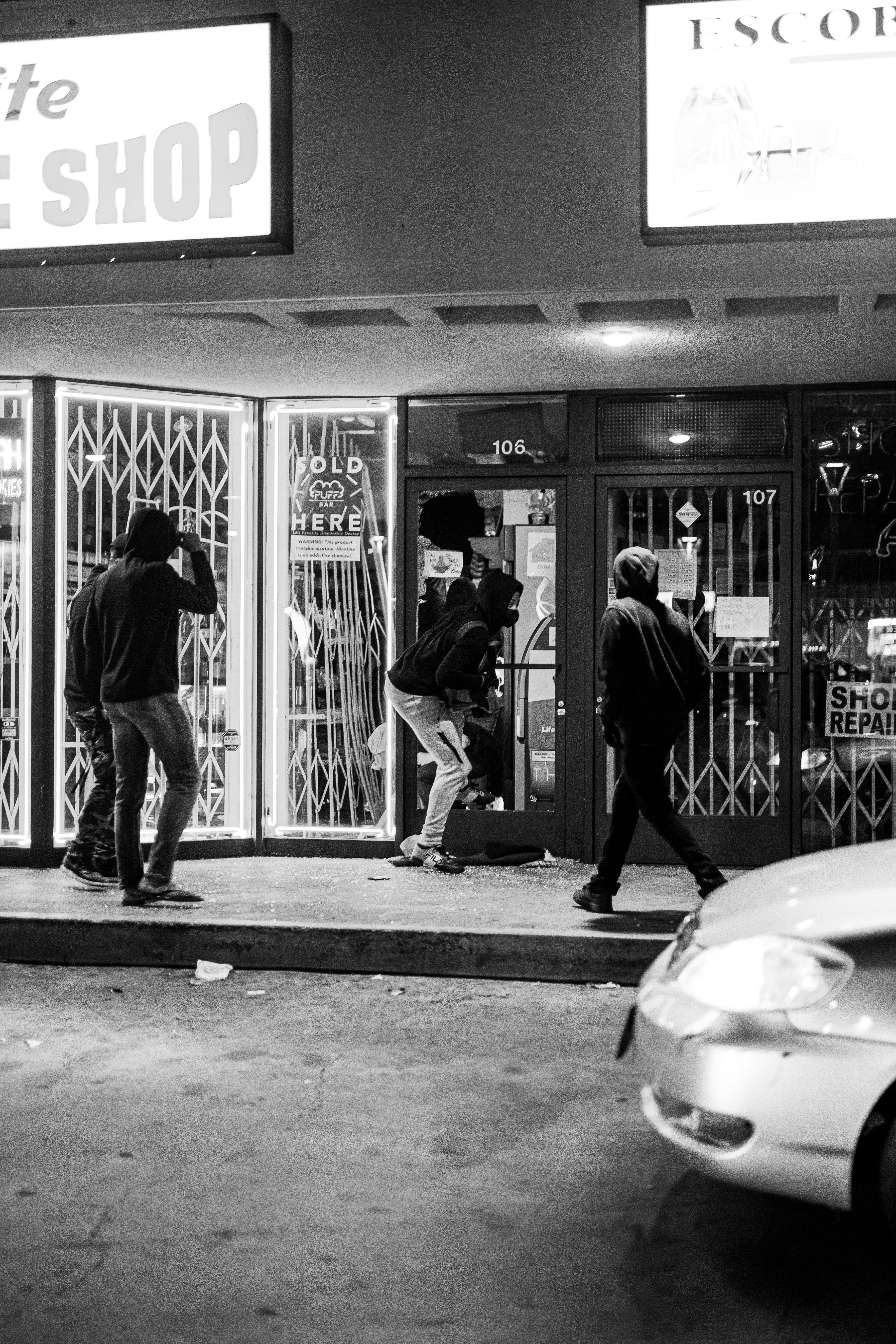 grayscale photo of man in black jacket and pants walking on sidewalk