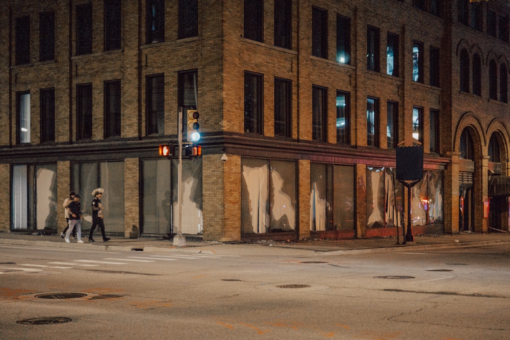 夜間に茶色のコンクリートの建物の近くの歩道を歩く人々
