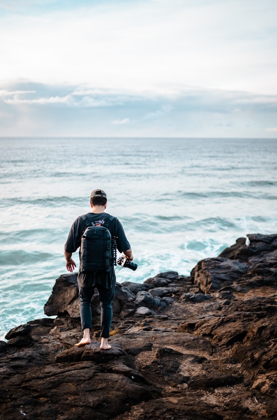 man in black jacket and black pants standing on rocky shore during daytime in Fingal Head Australia