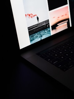 An open laptop displaying a collage of images on its screen. One of the images shows a silhouetted person standing on a structure with red smoke in the background. Another image features a bridge over a body of water, bathed in a warm, pinkish light.
