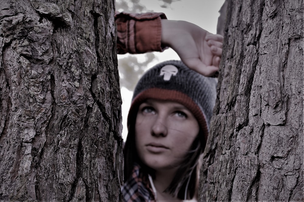 boy in gray knit cap and gray sweater leaning on brown tree