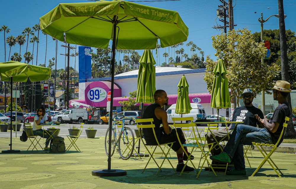 man in black t-shirt sitting on chair under green umbrella during daytime