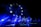 A band performs on stage under vibrant blue lighting, creating a dramatic atmosphere. The backdrop features stars, reminiscent of a flag design, adding to the visual impact of the scene. The musicians appear silhouetted due to the intense lighting coming from behind.