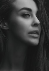 A grayscale portrait of a woman looking to the side, capturing a thoughtful and serene expression on her face. The lighting highlights her facial features and smooth skin, giving the image a soft and elegant appearance.