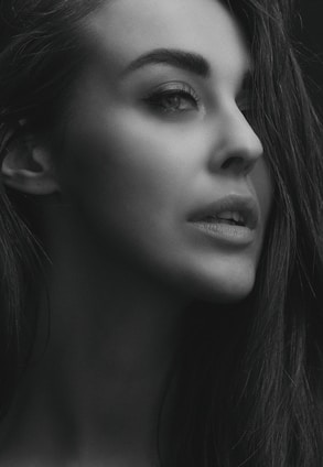 A grayscale portrait of a woman looking to the side, capturing a thoughtful and serene expression on her face. The lighting highlights her facial features and smooth skin, giving the image a soft and elegant appearance.