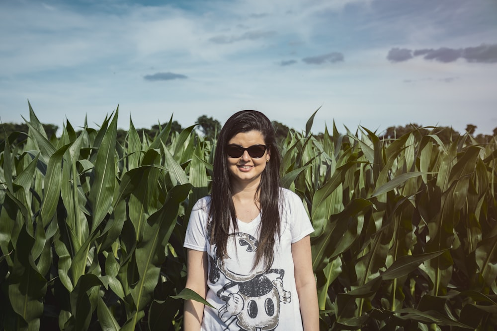 woman in white and black floral shirt wearing black sunglasses standing in corn field during daytime