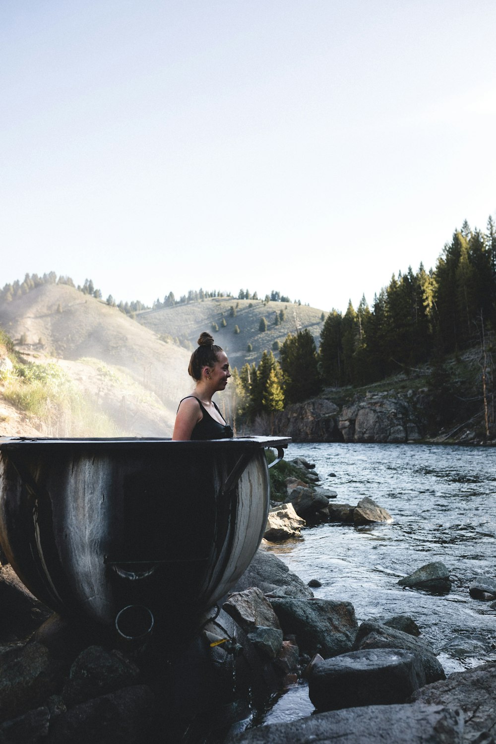 woman in black tank top sitting on gray rock near river during daytime