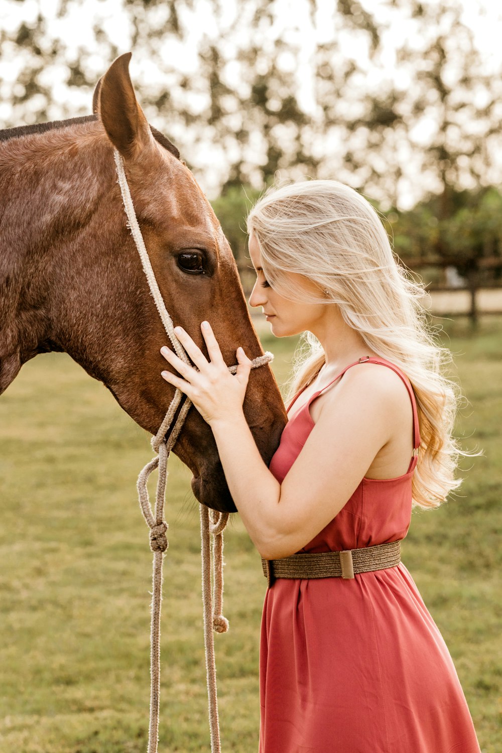 femme en robe rouge debout à côté d’un cheval brun pendant la journée