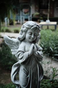 Statue d’ange en pierre grise dans un jardin, symbole de soin et d’accompagnement.