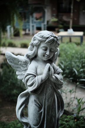 Statue d’ange en pierre grise dans un jardin, symbole de soin et d’accompagnement.