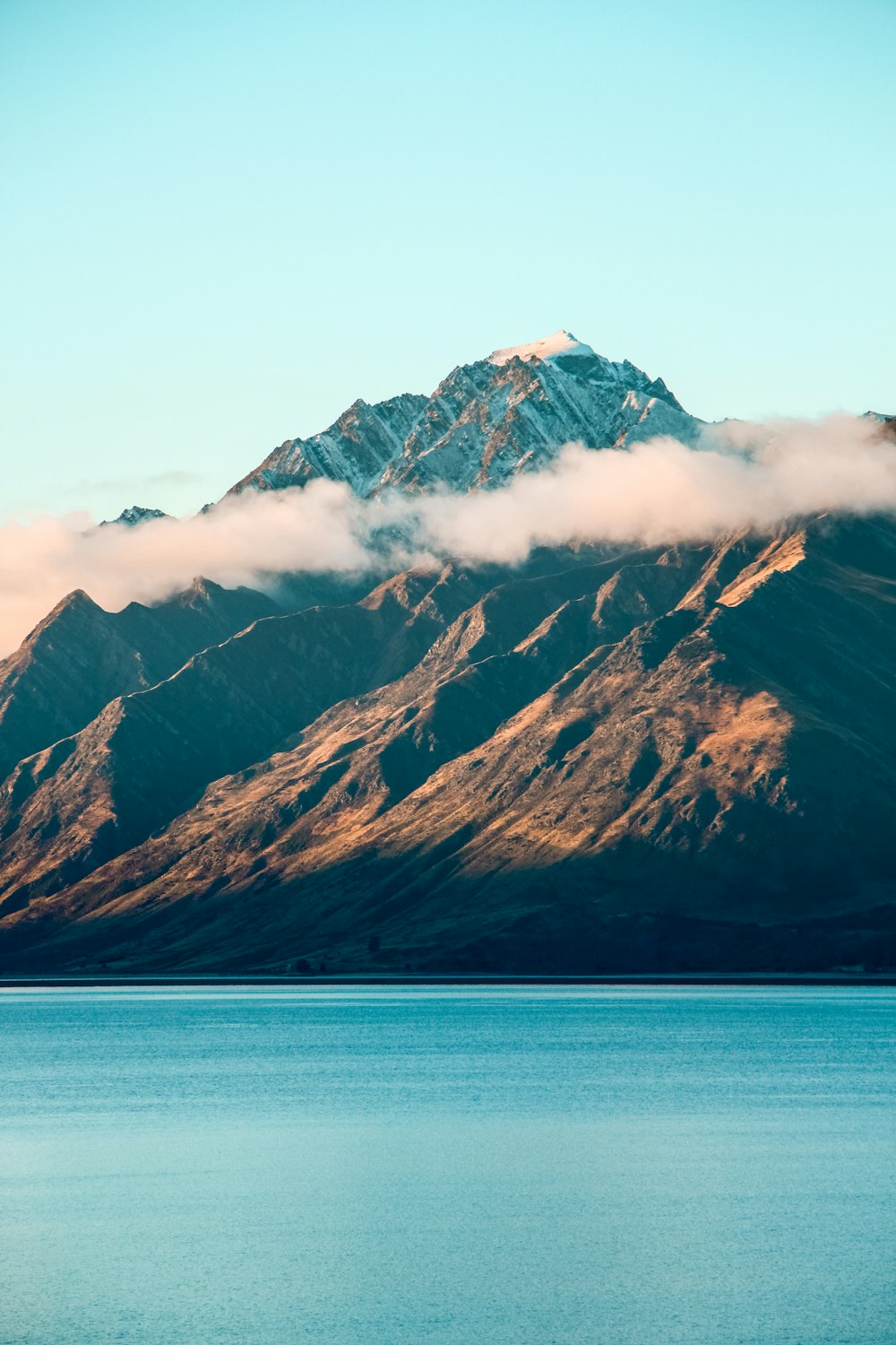 snow covered mountain beside body of water during daytime