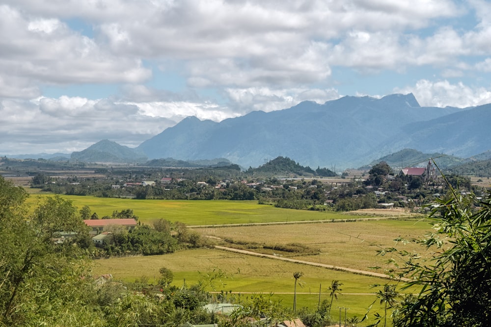 green grass field near mountains under white clouds during daytime