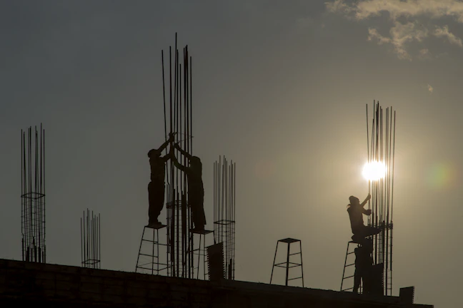Construction workers setting steel reinforcements on a large infrastructure project site during sunset.