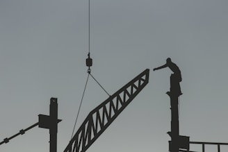silhouette of man standing on top of tower crane