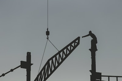 silhouette of man standing on top of tower crane