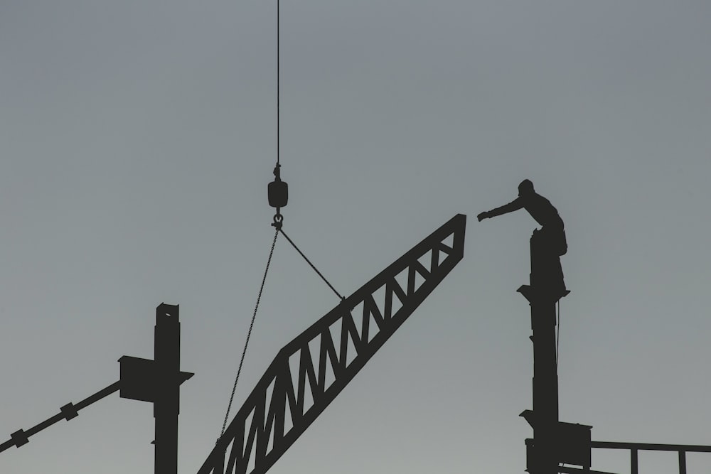 silhouette of man standing on top of tower crane