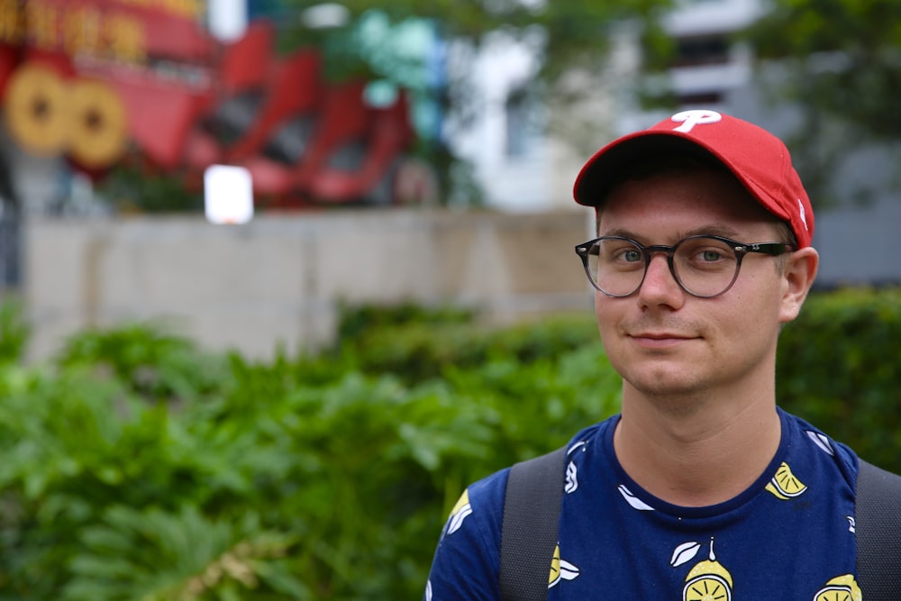 Garçon en chemise à col rond bleu et jaune portant des lunettes à monture noire et une casquette rouge