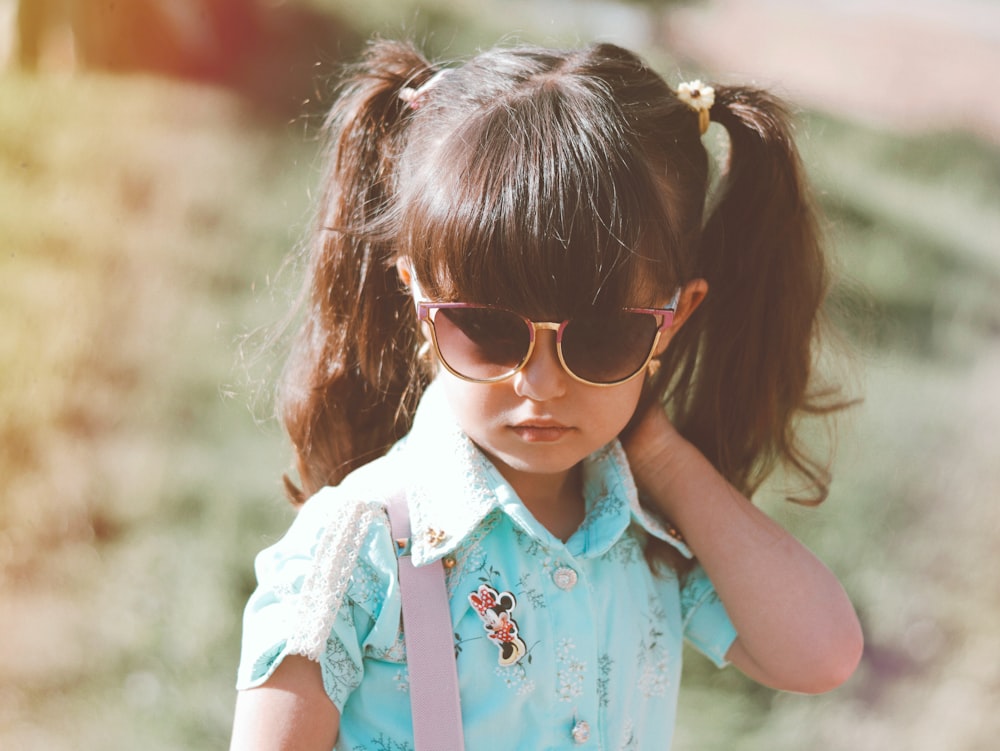 menina na camisa floral azul e branca que veste óculos de sol castanhos