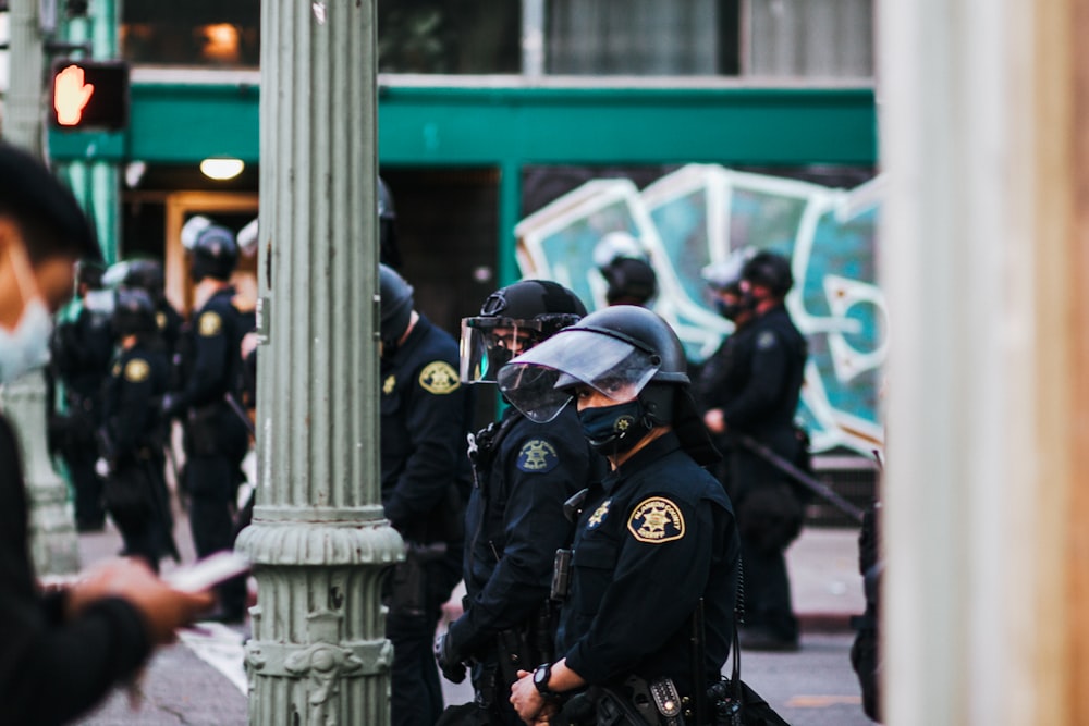 uomo in uniforme nera della polizia in piedi vicino al palo di cemento bianco durante il giorno