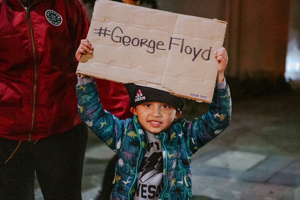 Un ragazzino che regge un cartello che dice George Floyd