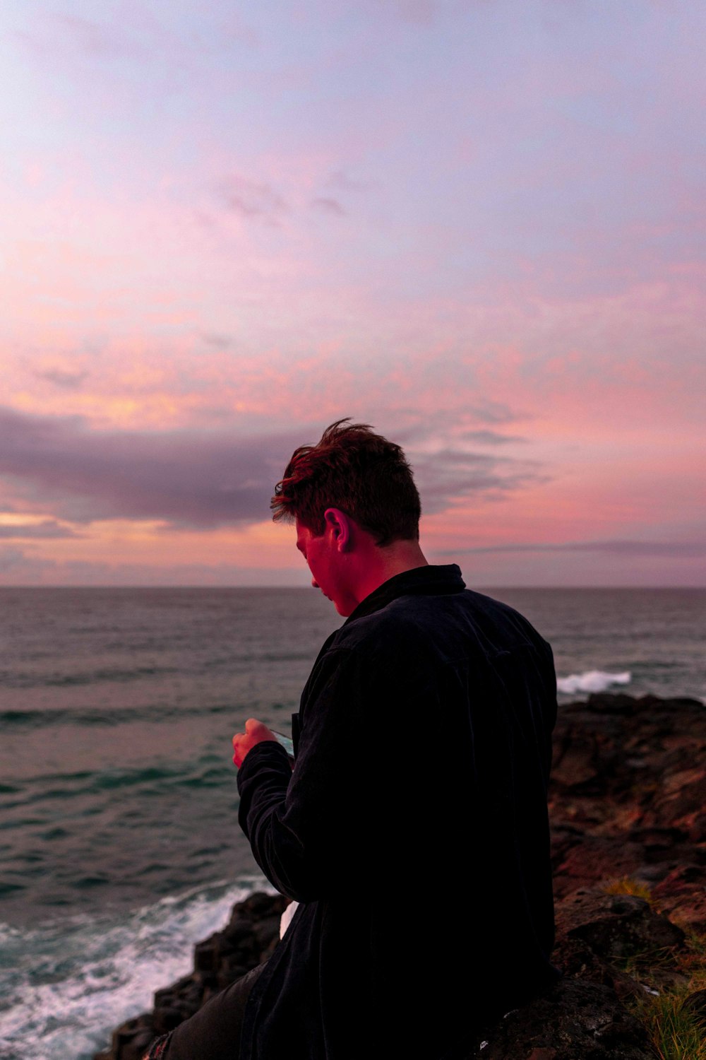 man in black jacket standing on brown rock near body of water during daytime