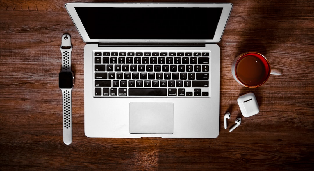 macbook pro beside white ceramic mug on brown wooden table