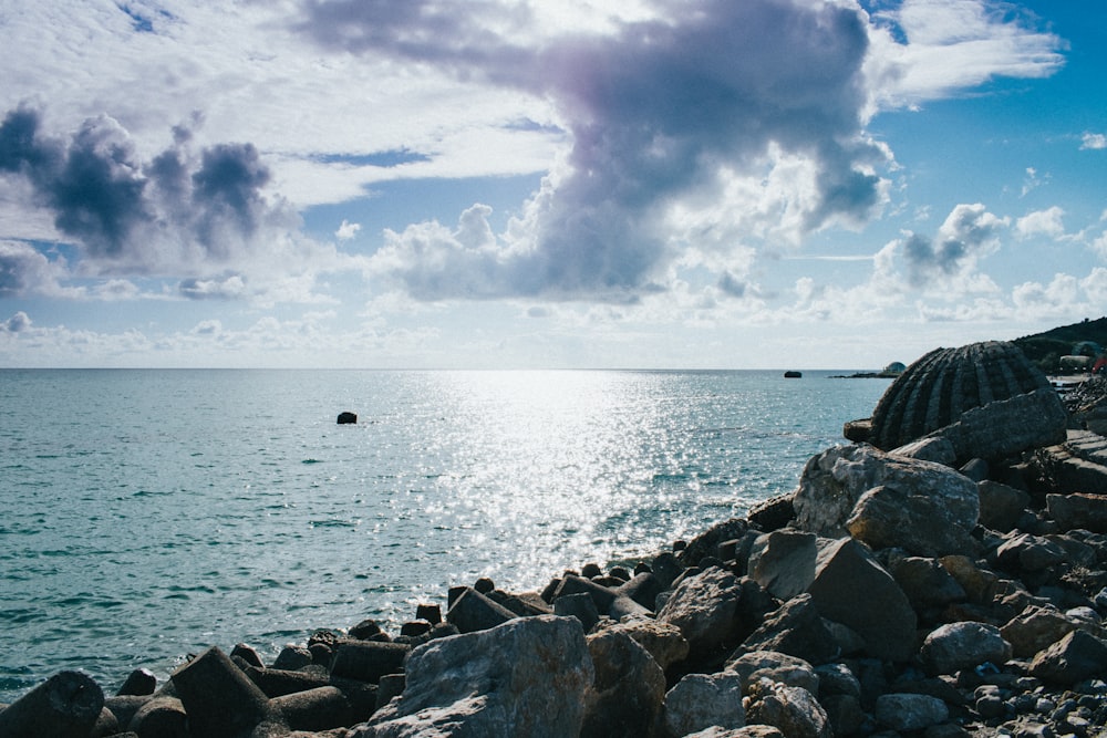 gray rocks near body of water under white clouds and blue sky during daytime