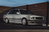 A classic white sedan with vintage charm, parked beside a rustic wooden fence.