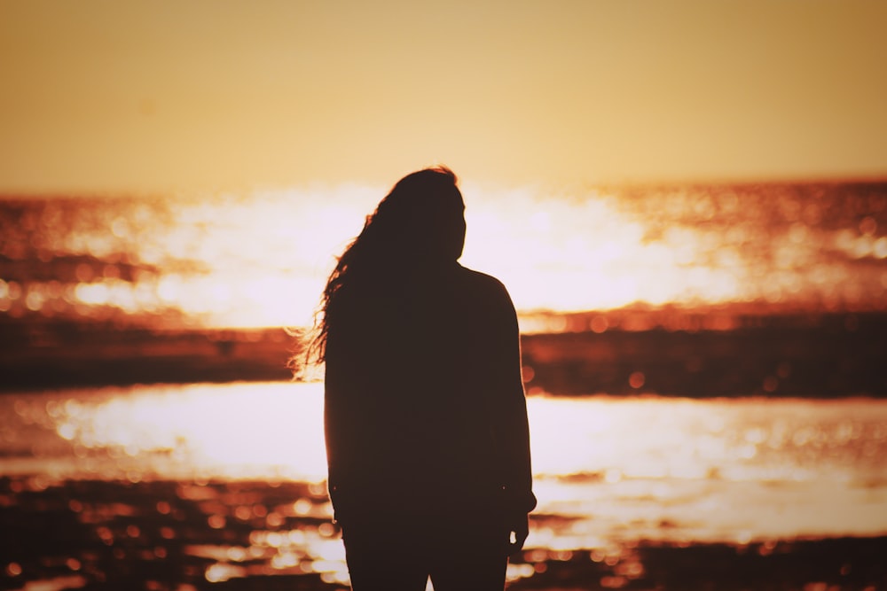 silhouette of woman standing on seashore during sunset