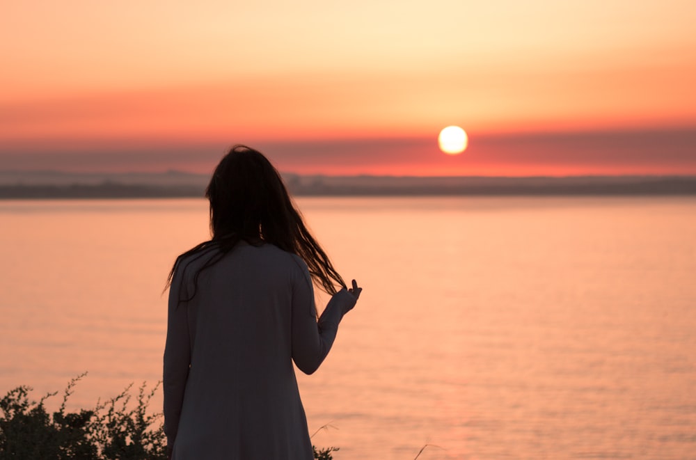 woman in white dress standing near body of water during sunset
