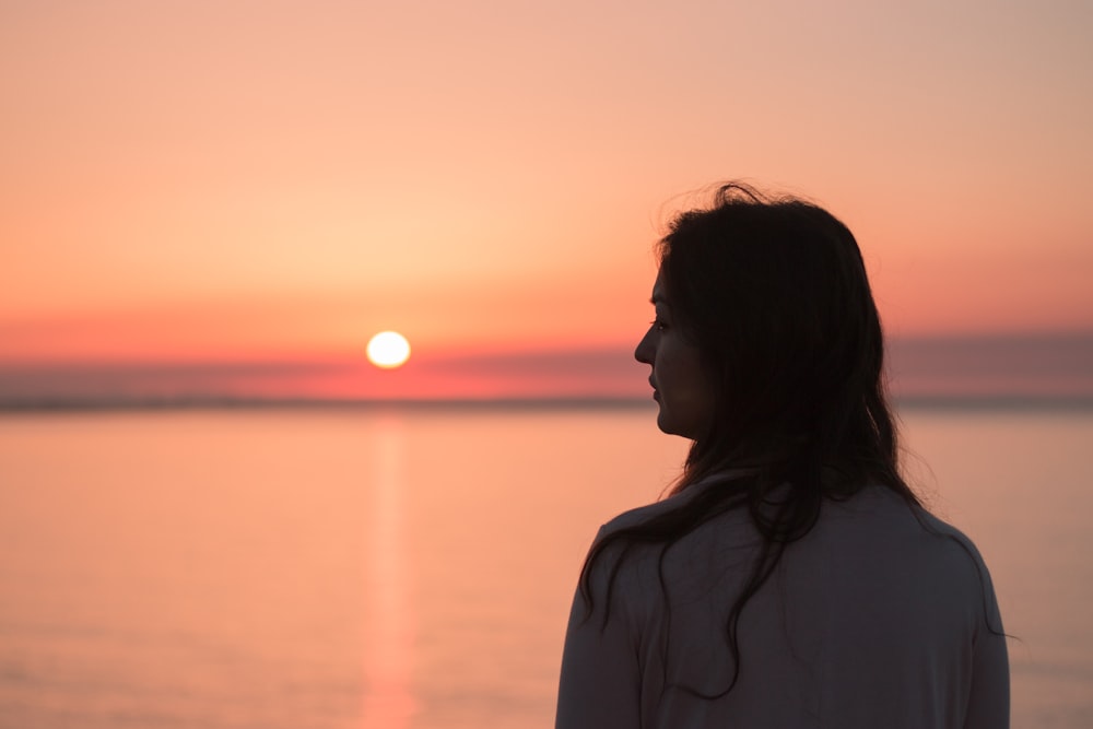 woman in white shirt standing near body of water during sunset