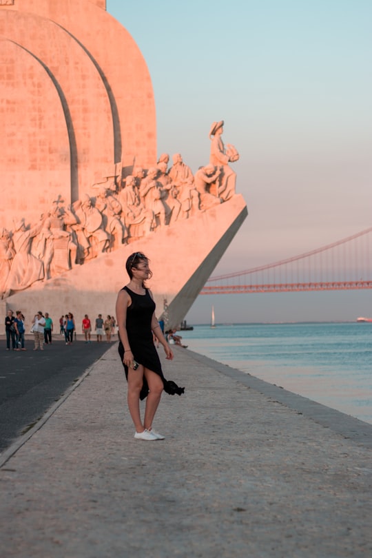 woman in black tank top and black skirt standing on gray concrete floor near body of near near near near in Padrão dos Descobrimentos Portugal