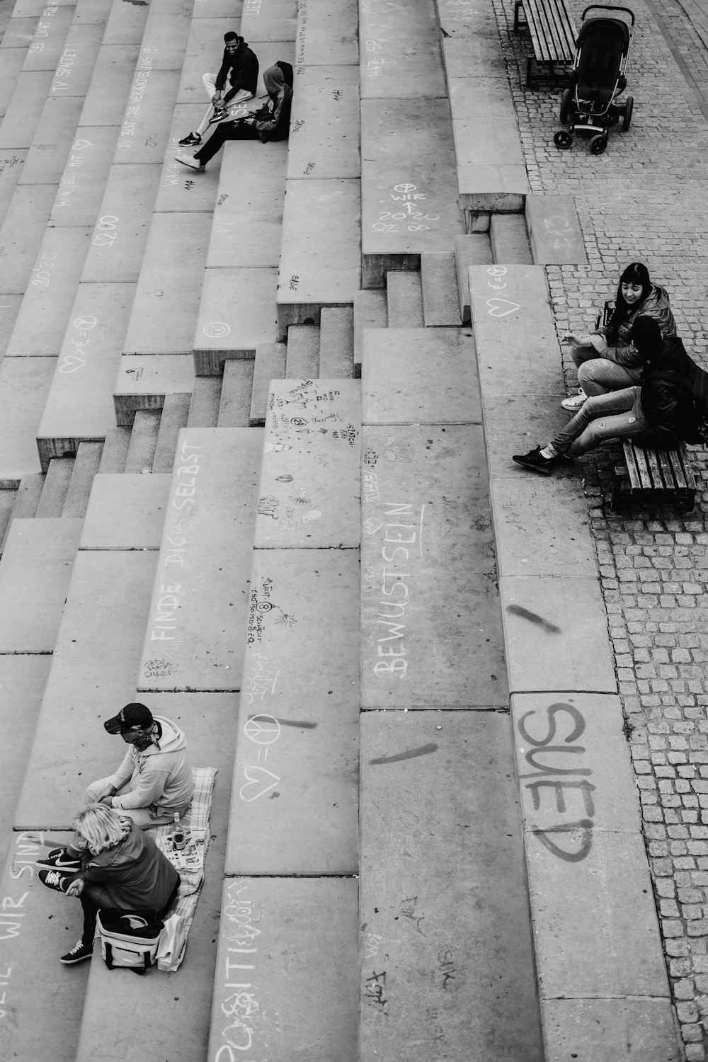 man in black jacket sitting on concrete pavement