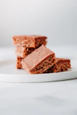 Close-up of a fudgy brownie with a glossy chocolate crust on a minimalist beige plate.