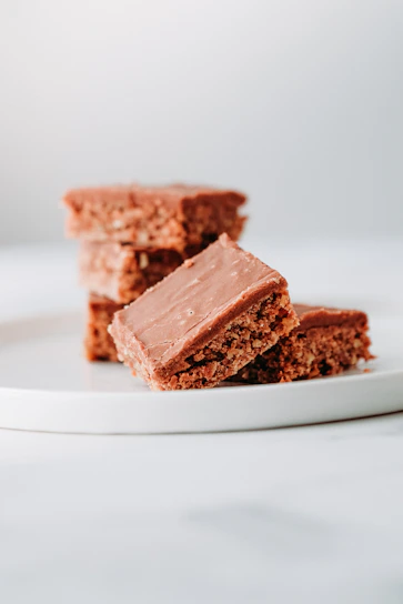 Close-up of a stack of fudgy, glossy brownies with a sprinkle of sea salt on top, set on a minimalist beige plate.