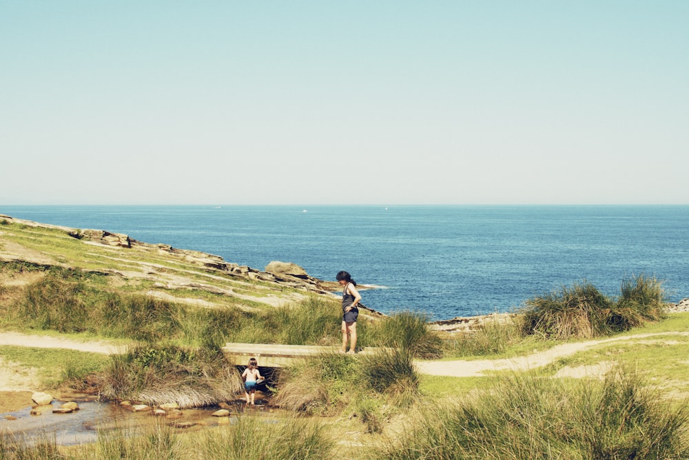 2 person standing on green grass field near body of water during daytime