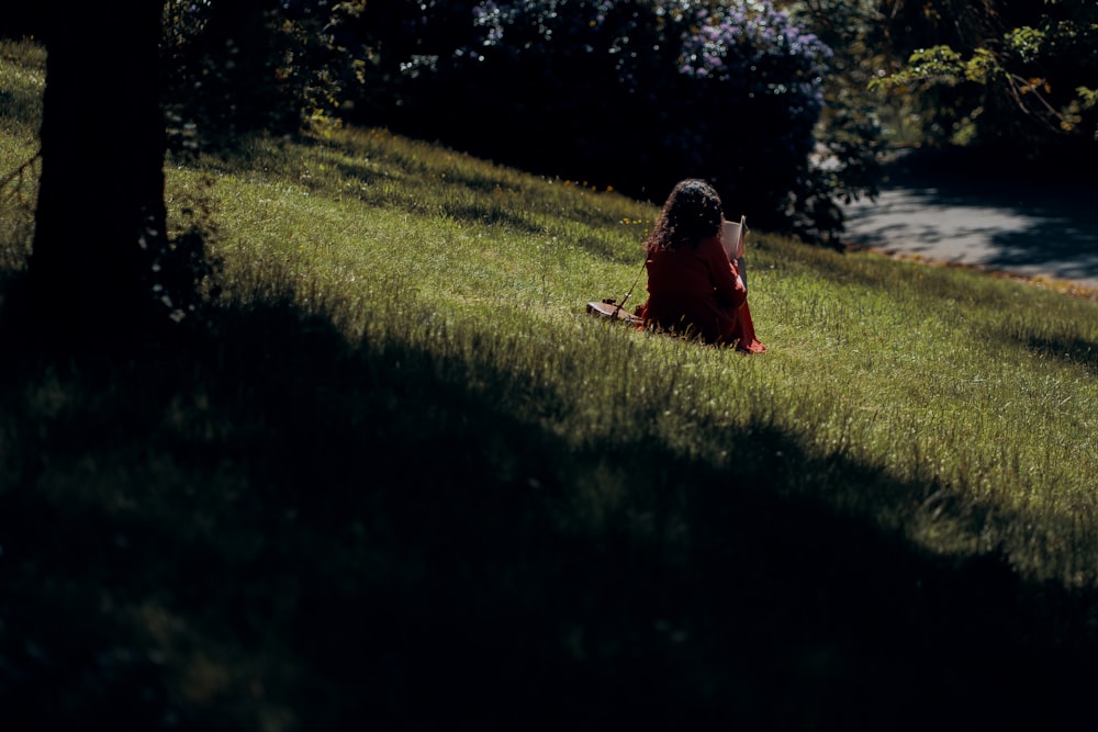 woman in red dress sitting on green grass field during daytime