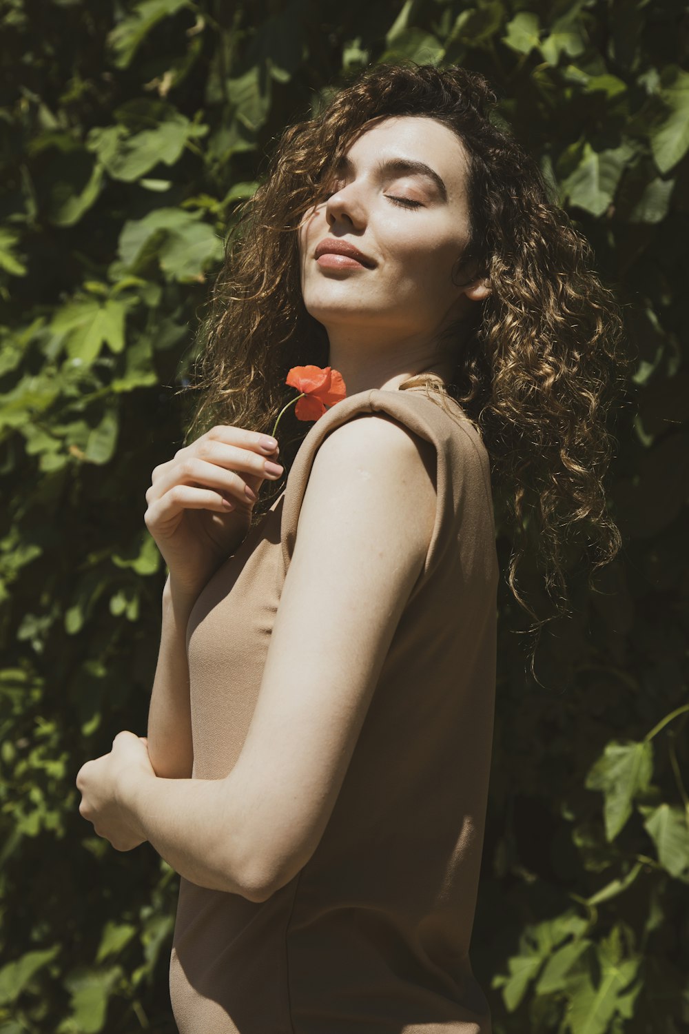 Femme en débardeur marron tenant une rose rouge