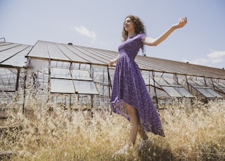girl in purple dress standing on brown grass field during daytime
