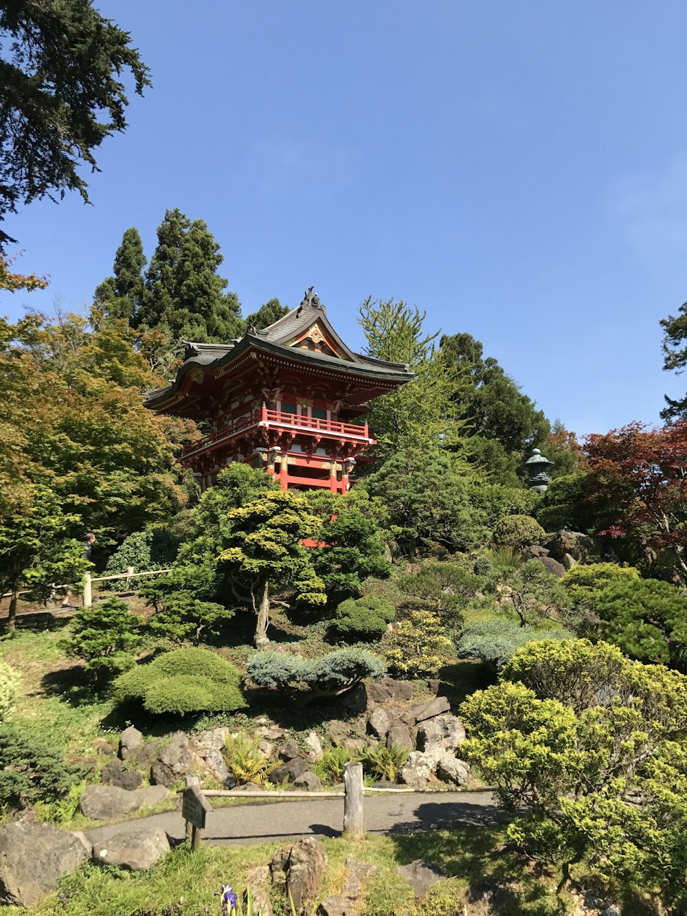 昼間は青空の下、緑の木々に囲まれた赤と黒のパゴダ寺院