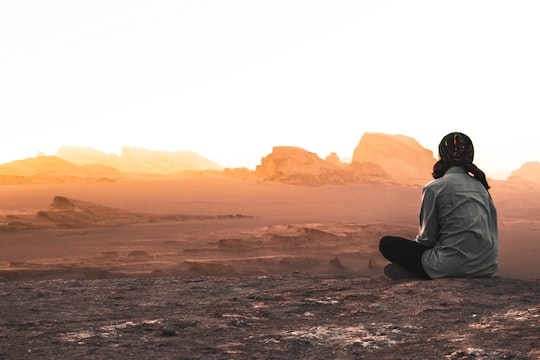 man in white long sleeve shirt sitting on gray sand during daytime in Shahdad Iran