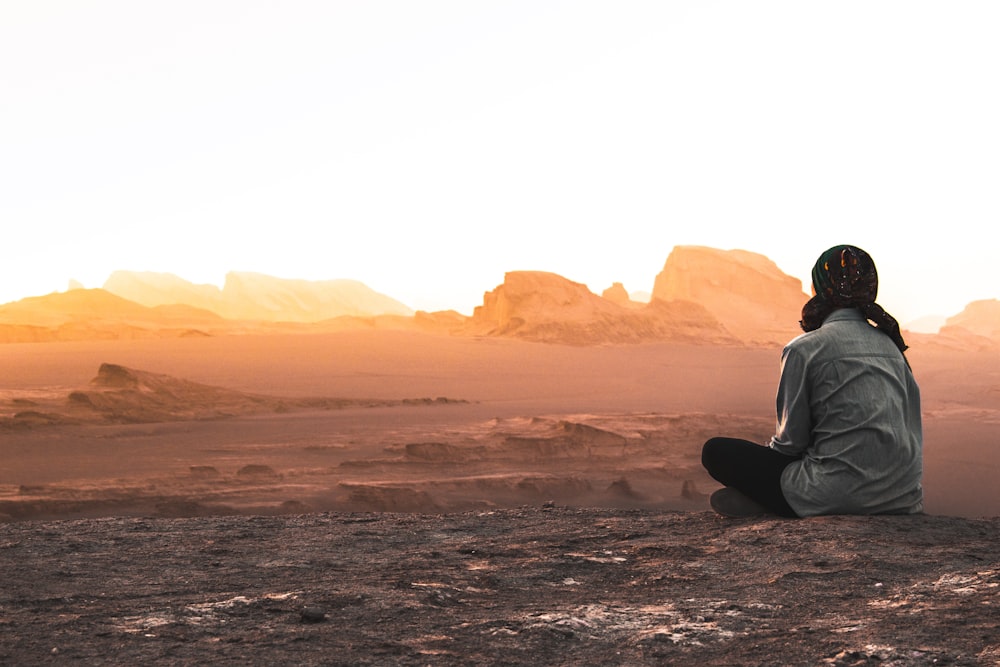 man in white long sleeve shirt sitting on gray sand during daytime