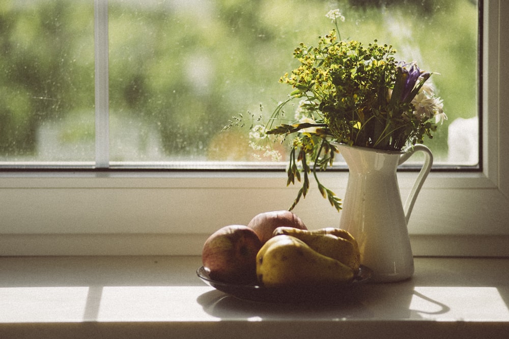 green plant in white ceramic vase beside red apple fruit