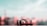 A small, toy car is positioned on a flat surface with a blurred, pastel-colored background. The toy car is detailed with markings and has an aerodynamic design. The scene is softly lit, creating a dreamy atmosphere.