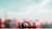 A small, toy car is positioned on a flat surface with a blurred, pastel-colored background. The toy car is detailed with markings and has an aerodynamic design. The scene is softly lit, creating a dreamy atmosphere.