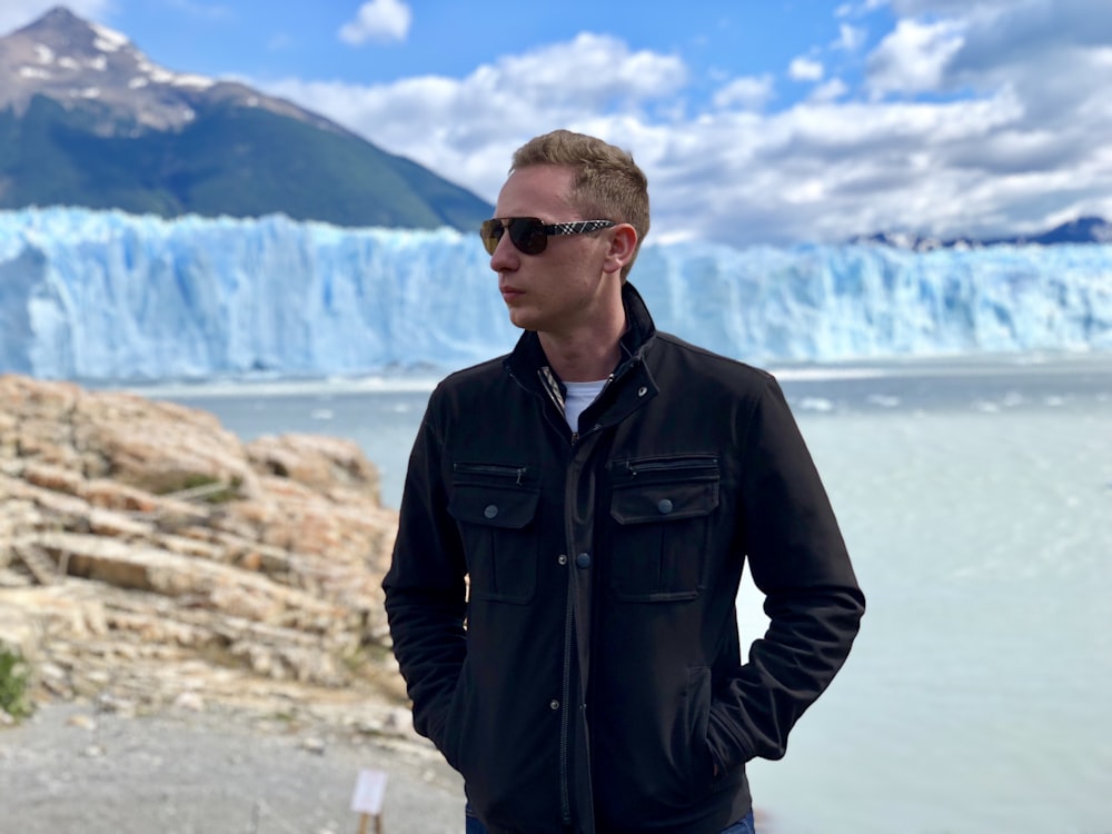 man in black leather jacket standing on gray rock during daytime